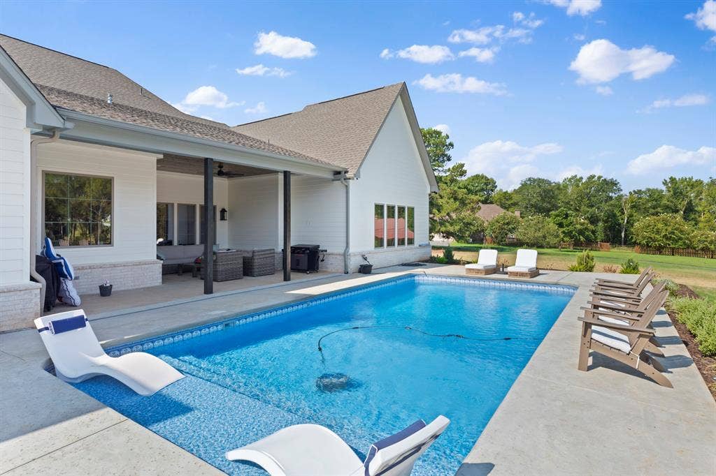 23180 Bridle View Drive, Lindale, TX 75771 Outdoor pool with an integrated sun shelf, concrete decking, and a covered patio featuring dark columns and a shingle roof