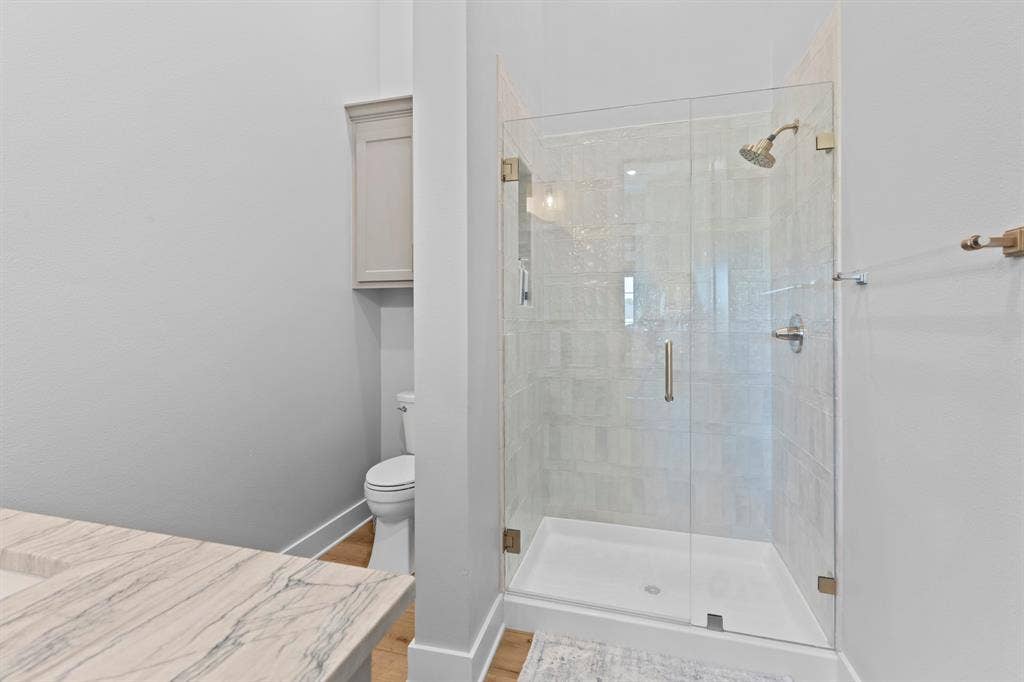 23180 Bridle View Drive, Lindale, TX 75771 Glass-enclosed shower with a tiled surround, built-in toilet, stone-finish countertop, and wood-finish flooring