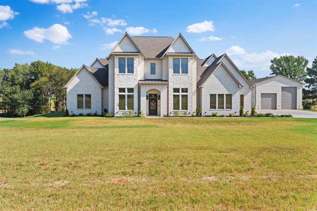 23180 Bridle View Drive, Lindale, TX 75771 White brick and stone exterior with a dark grey roof, featuring multiple gables and a large attached auxiliary building with two garage doors
