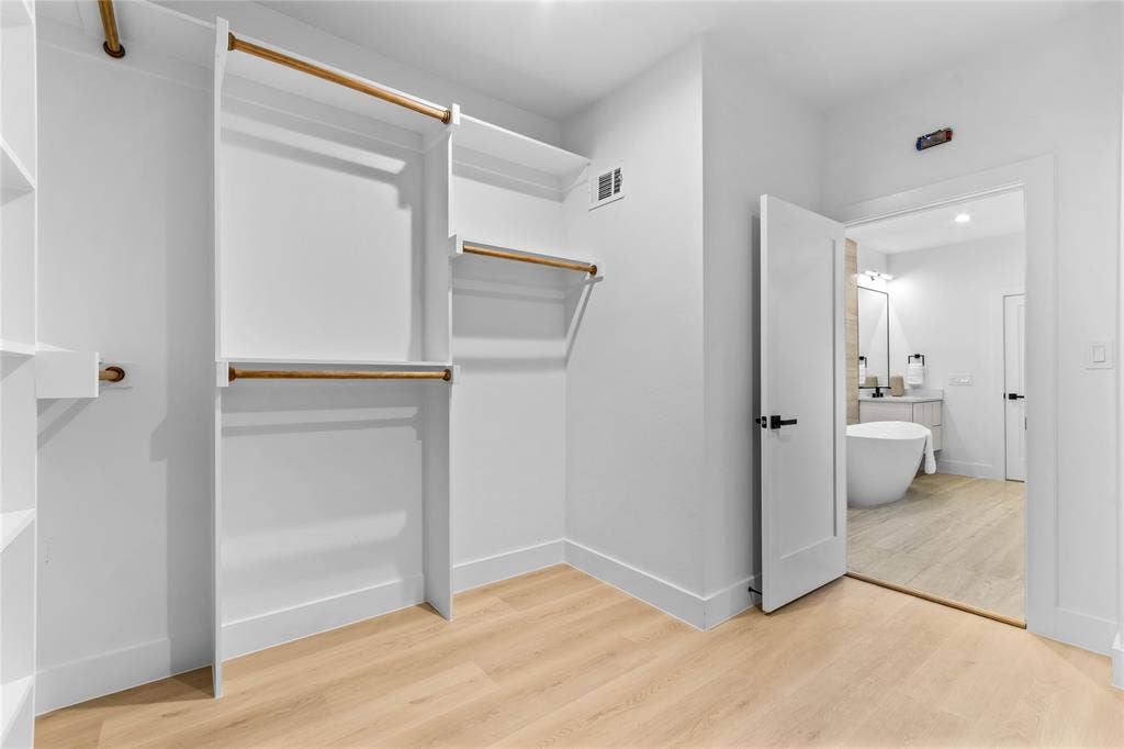 Walk-in closet featuring white built-in shelving, hanging rods, and light wood-finish flooring