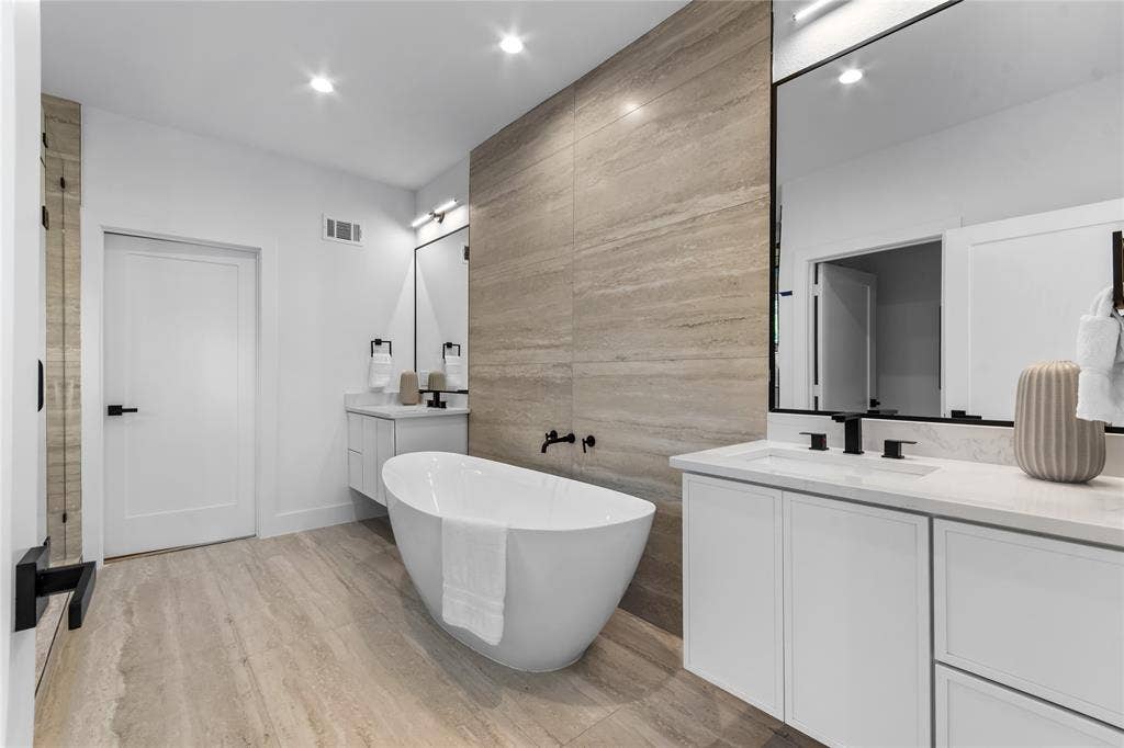 Freestanding soaking tub with a floor-mounted faucet, complemented by dual vanities with integrated sinks and matte black fixtures
