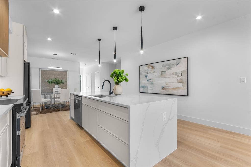 Contemporary kitchen featuring a spacious island with a waterfall countertop, integrated dishwasher, and under-mount sink with a matte black faucet