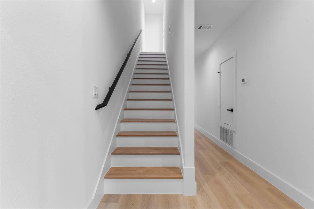 Staircase featuring wood-finish treads and white risers with a black wall-mounted handrail