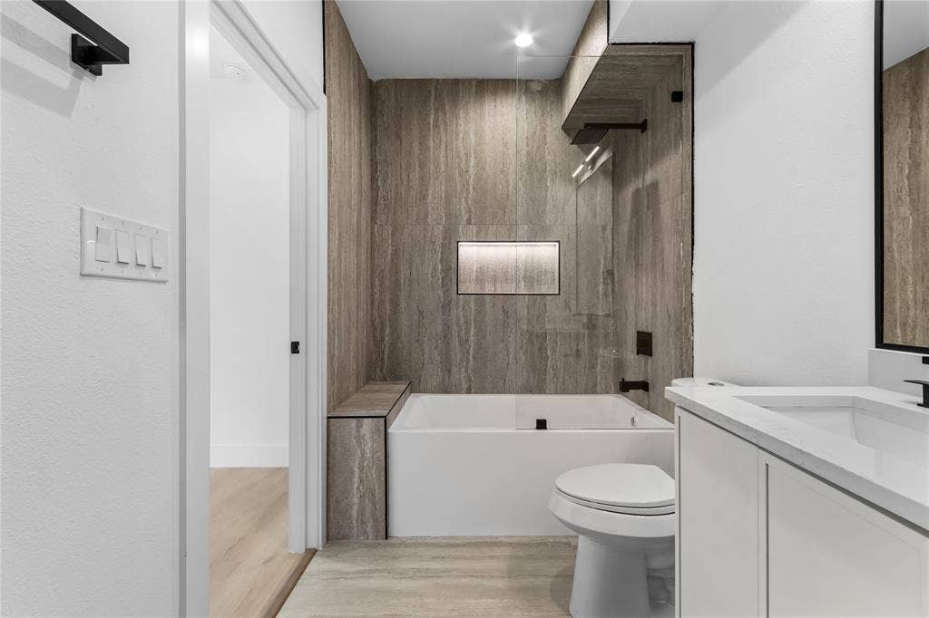 Contemporary bathroom featuring a tub and shower combination with full-height stone-look tile surround, a built-in bench, and an illuminated shower niche