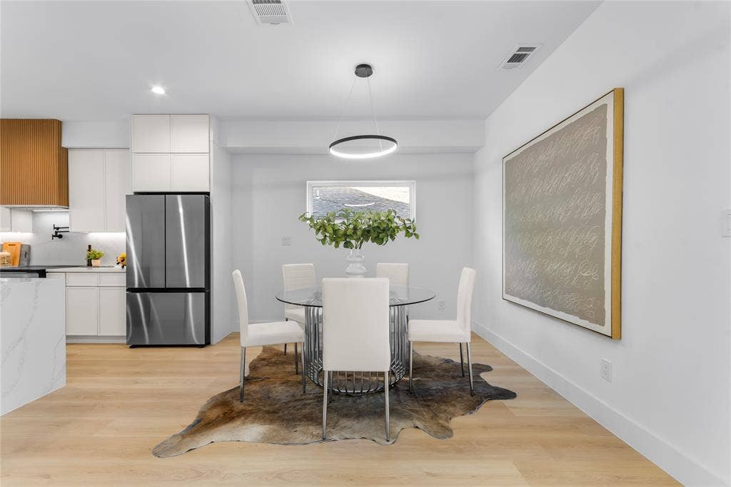 Open-concept living space featuring wood-finish flooring, a contemporary circular chandelier, and a kitchen with two-tone cabinetry and stainless-steel appliances