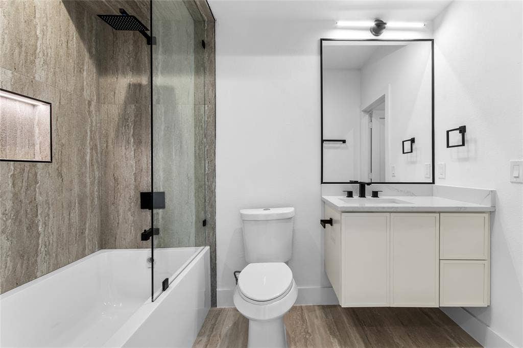 Sleek bathroom featuring a floating vanity with a stone countertop, a rectangular mirror with a black frame, and a tub-shower combination with a glass panel and matte black fixtures