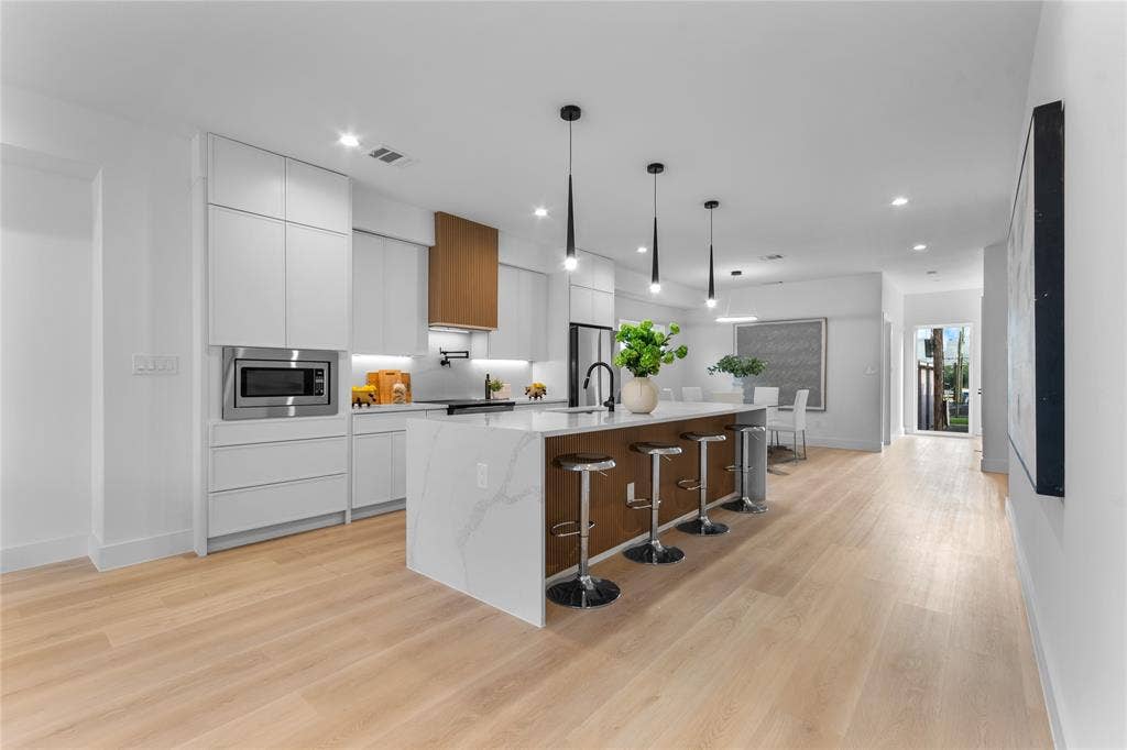 Gourmet kitchen featuring a waterfall island with integrated seating, stainless steel microwave, light wood-finish flooring, and pendant lighting