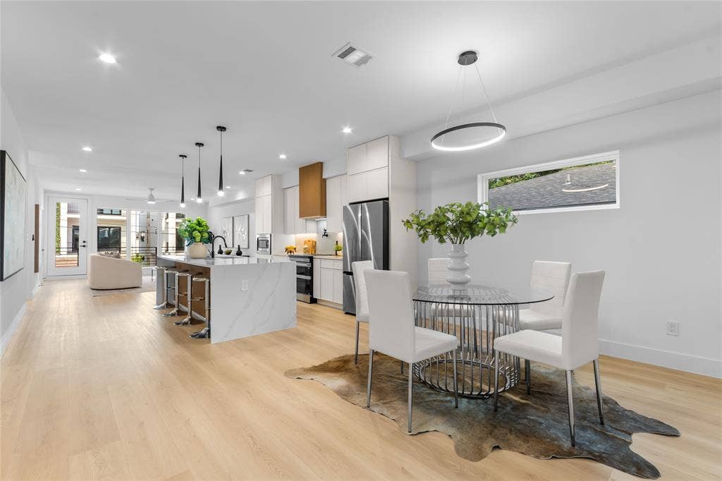 Open-concept living space featuring light wood-finish flooring, recessed lighting, a kitchen island with seating, a range hood, and a dining area with a modern chandelier
