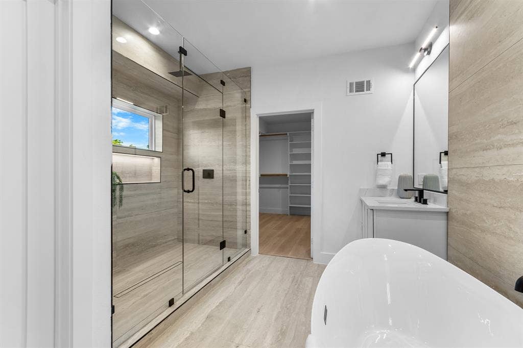 Spacious bathroom featuring a glass-enclosed shower with stone-look tile, integrated shelving, and a window