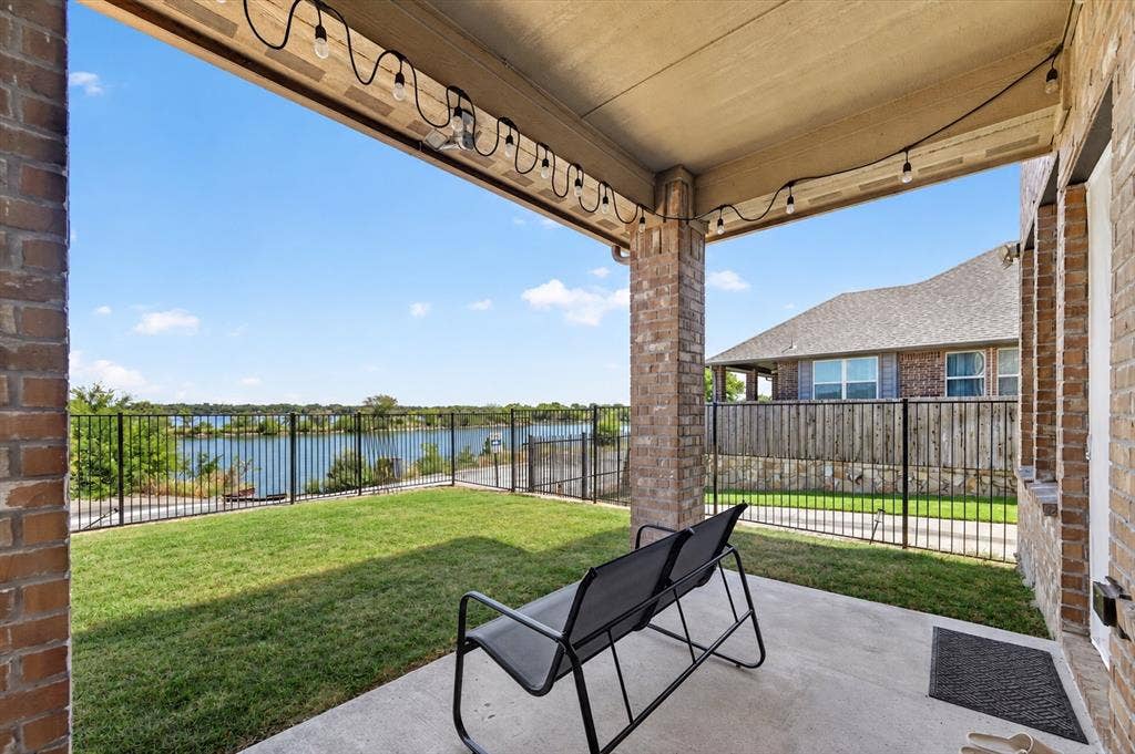 2025 Lake Front Trail, Garland, TX 75043 Covered patio with concrete flooring, brick columns, and a grassy area enclosed by a black metal fence