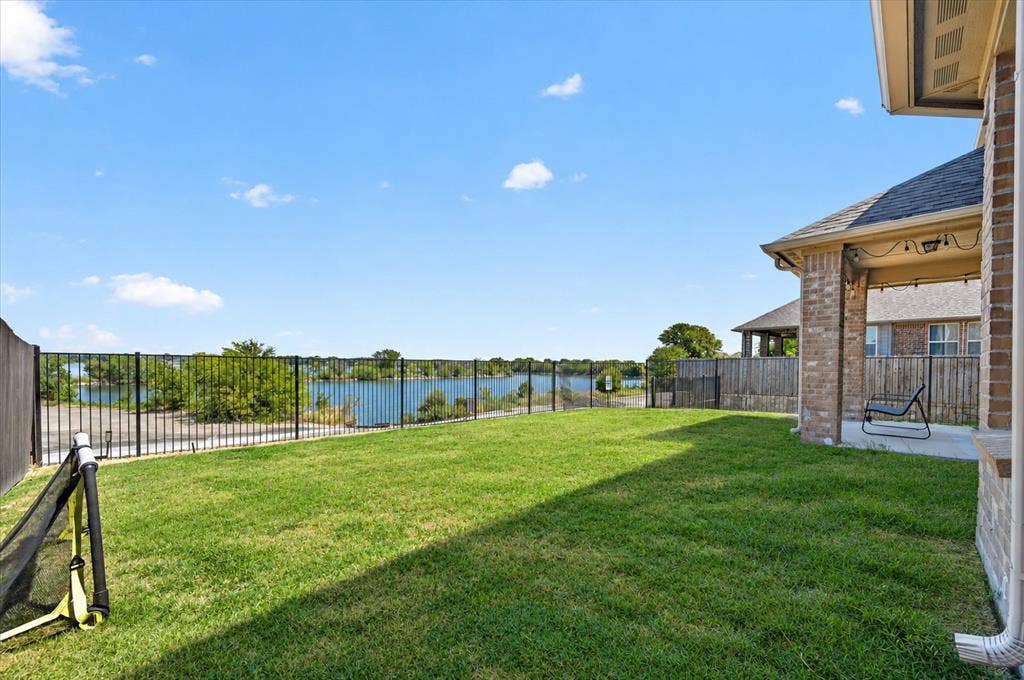 2025 Lake Front Trail, Garland, TX 75043 Expansive green lawn with a black metal fence, covered patio with string lights, and brick exterior
