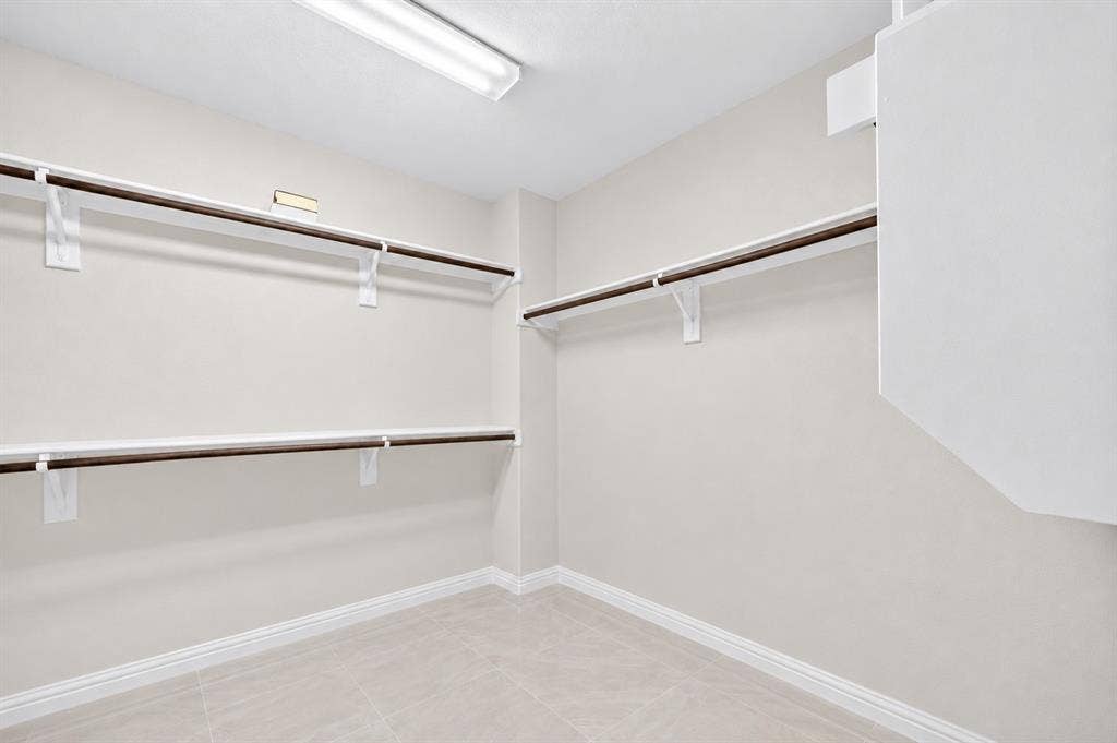 2025 Lake Front Trail, Garland, TX 75043 Recessed lighting illuminates a spacious closet featuring multiple hanging rods and shelving, complemented by light-toned tile flooring