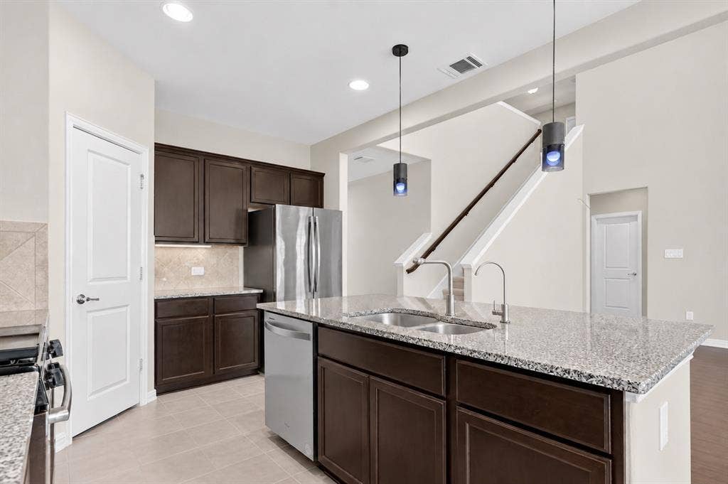 2025 Lake Front Trail, Garland, TX 75043 Kitchen island with dual stainless steel sinks, granite countertops, dark wood-finish cabinetry, and stainless steel appliances