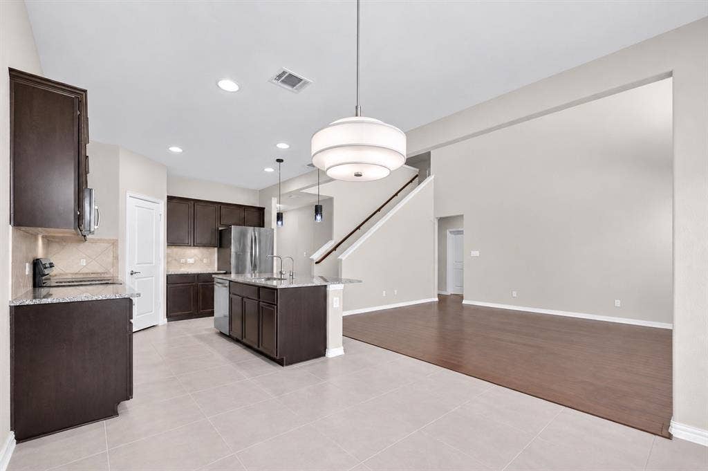 2025 Lake Front Trail, Garland, TX 75043 Kitchen featuring dark wood cabinetry, light-toned tiled flooring, a central island with a sink, and stainless steel appliances