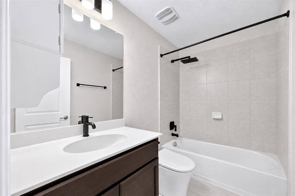 2025 Lake Front Trail, Garland, TX 75043 Bathroom featuring a dark wood-finish vanity, white countertop with integrated sink, black-finish faucet, and a tiled shower/tub combination with a black-finish shower head