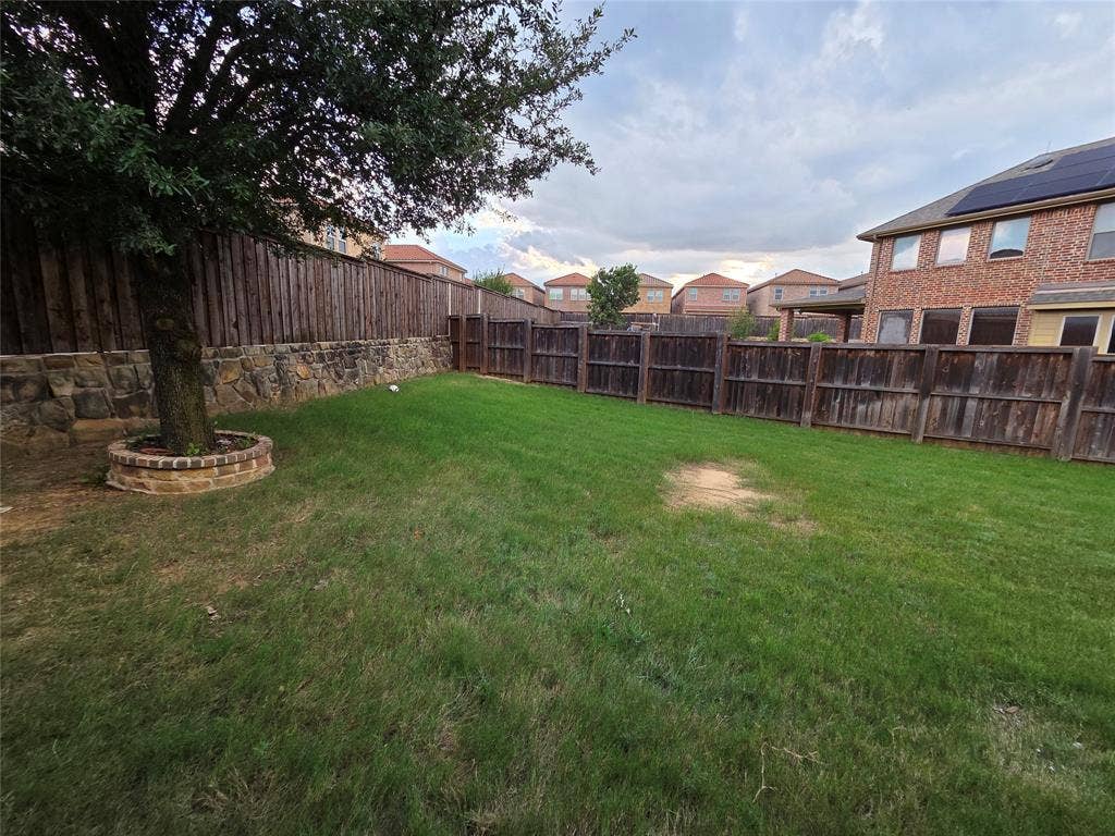 146 Rolling Fork Bend, Irving, TX 75039 Expansive backyard featuring a manicured lawn, established tree, and a stone retaining wall with brick accents