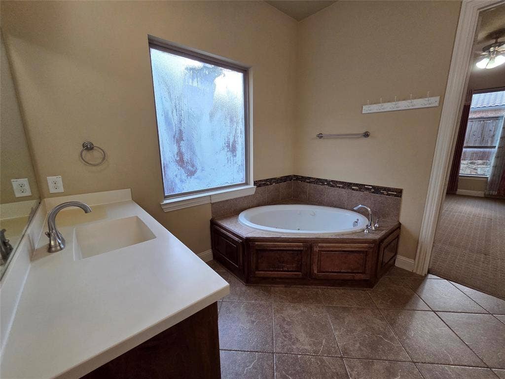 146 Rolling Fork Bend, Irving, TX 75039 Built-in corner bathtub with tiled surround, wood-finish cabinetry, and a single vanity with an integrated sink and light-toned countertop