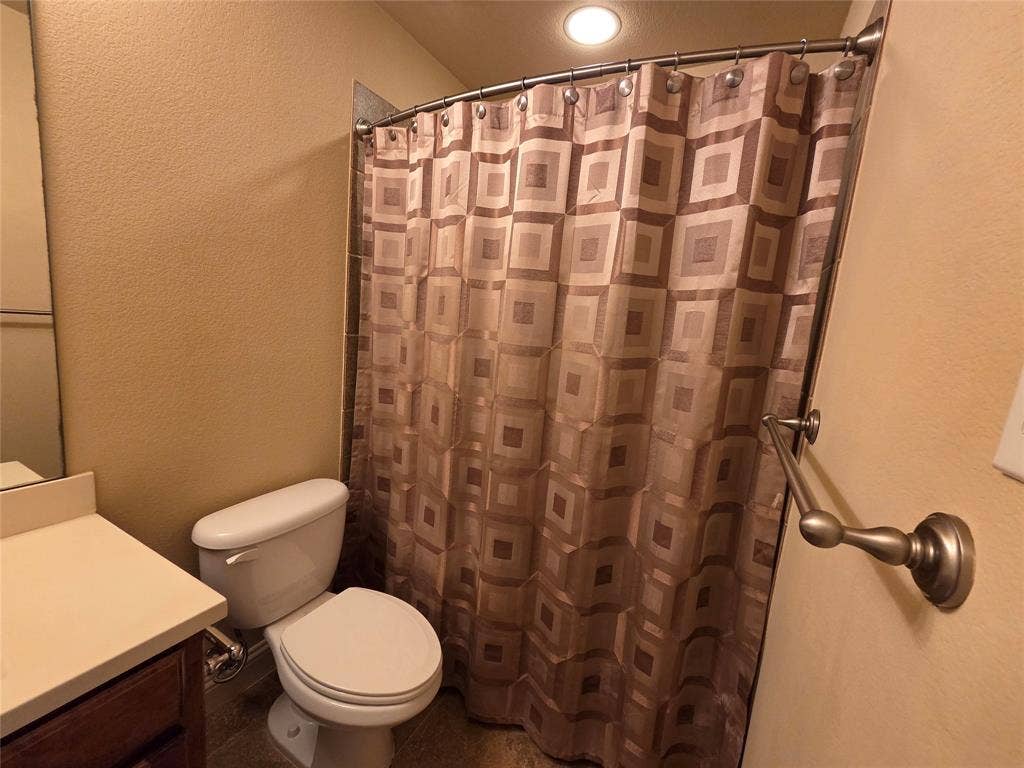 146 Rolling Fork Bend, Irving, TX 75039 White toilet with a built-in tank, light-colored countertop, and a dark wood-finish vanity
