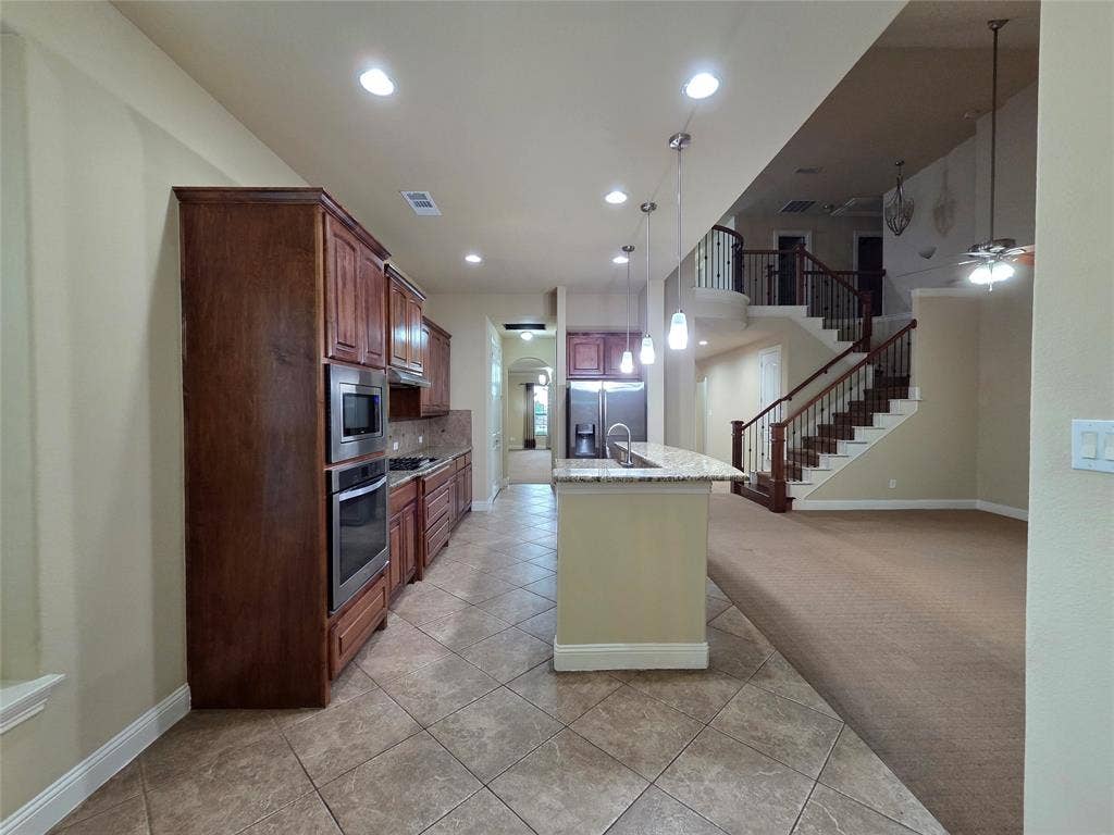 146 Rolling Fork Bend, Irving, TX 75039 Spacious kitchen featuring warm wood cabinetry, stainless steel appliances, and a central island with a sink and pendant lighting