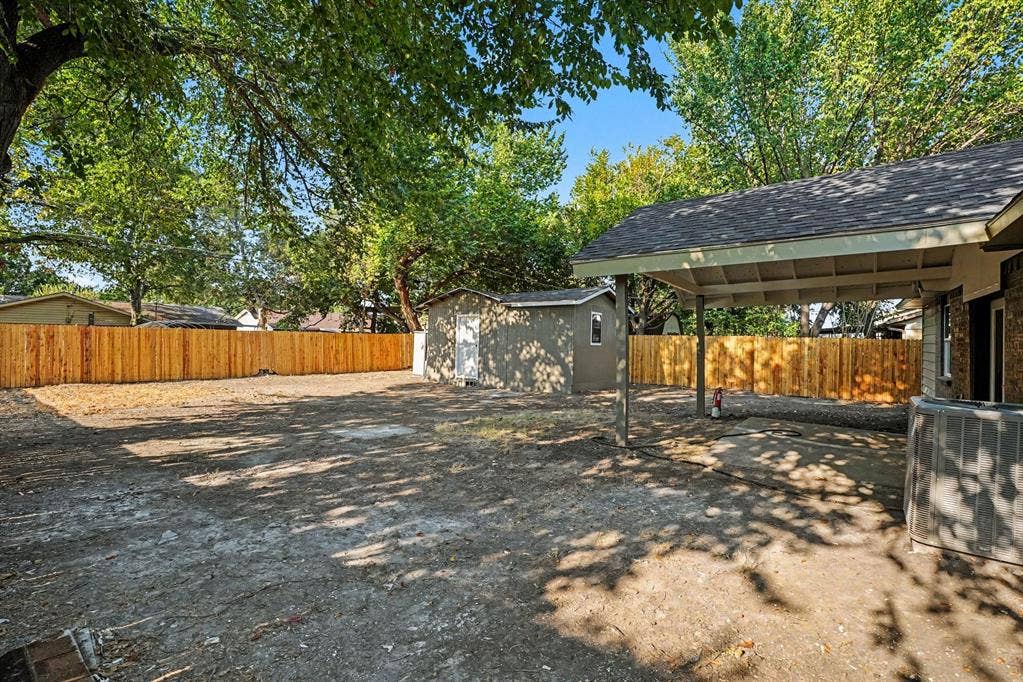 2429 February Lane, Grand Prairie, TX 75050 Spacious backyard with mature trees, new wood fencing, a dedicated storage shed, and a covered carport structure