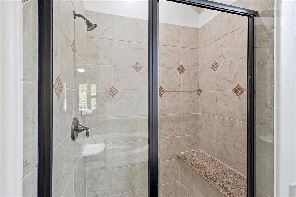 420 Silverado Trail, Keller, TX 76248 Tiled shower enclosure with a dark bronze showerhead, built-in soap dish, and a granite-topped shower bench
