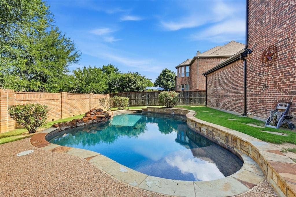 420 Silverado Trail, Keller, TX 76248 Curved swimming pool featuring a rock waterfall, stone coping, and exposed aggregate decking