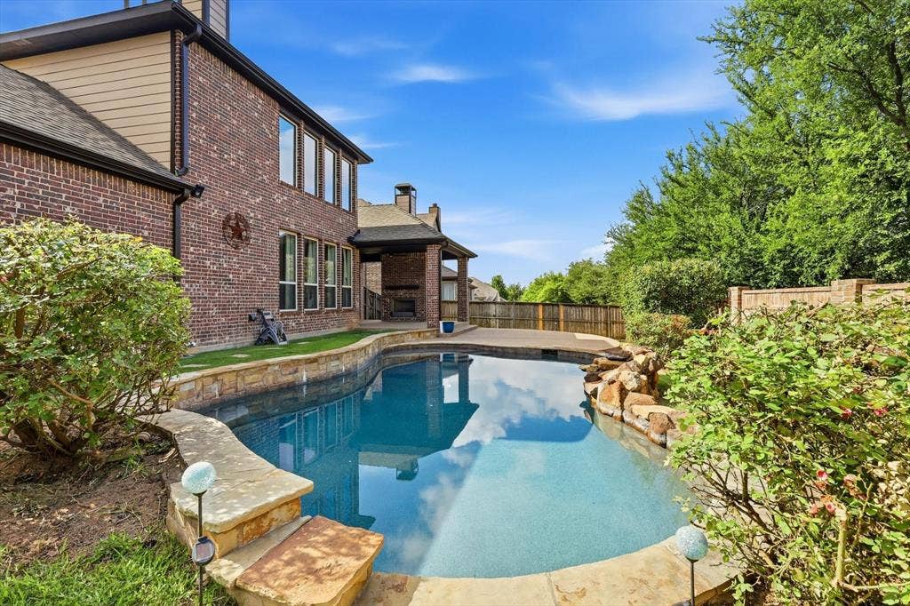 420 Silverado Trail, Keller, TX 76248 Curved swimming pool with stone coping, a rock water feature, a covered patio, and a brick exterior