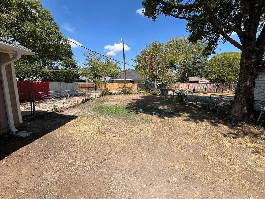 9615 Oak Gate Lane, Dallas, TX 75217 Spacious yard area enclosed by chain link fencing, featuring a mature shade tree and a portion of the property's exterior siding
