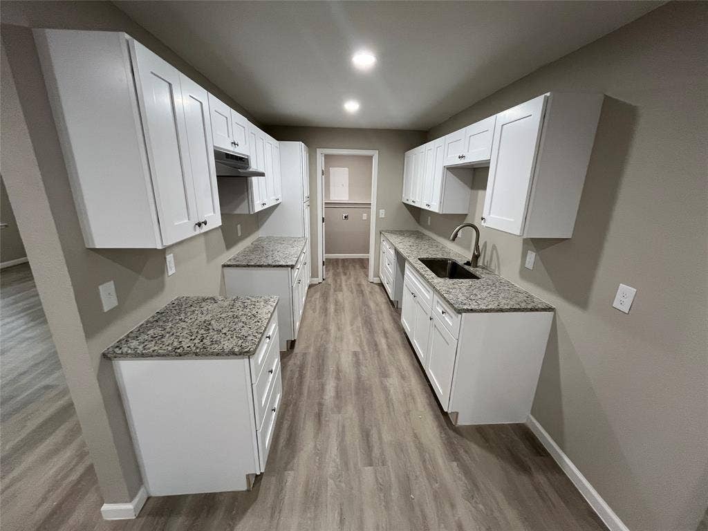 1831 Moonbeam Lane, Carrollton, TX 75006 Contemporary galley kitchen featuring white shaker-style cabinetry, granite-style countertops, a double basin sink with a high-arch faucet, and wood-finish flooring