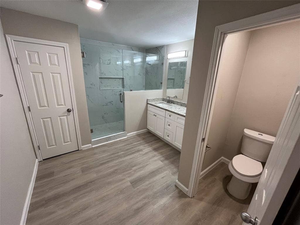 1831 Moonbeam Lane, Carrollton, TX 75006 Spacious bathroom featuring wood-finish flooring, a glass-enclosed shower with tile surround, a dual vanity with a light-toned countertop, and recessed lighting