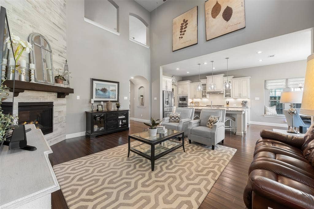 121 Lantana Lane, Wylie, TX 75098 Soaring ceilings with upper arched windows, wood-finish flooring, a stone-clad fireplace with a wood mantel, and an open-concept kitchen with white cabinetry