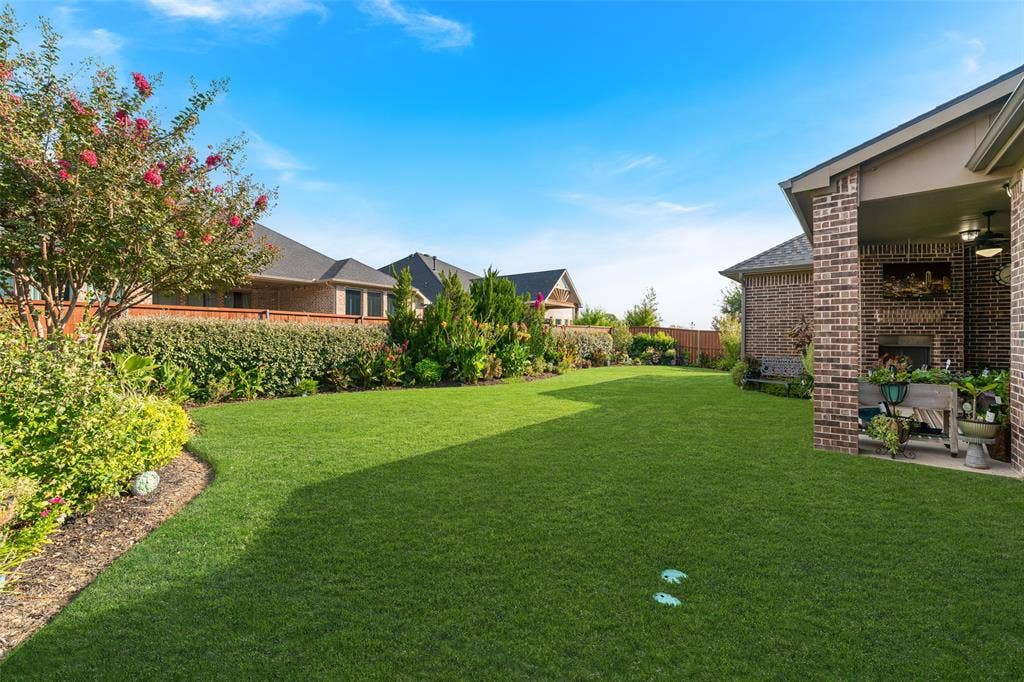 121 Lantana Lane, Wylie, TX 75098 Expansive backyard featuring a manicured lawn, established landscaping, and a covered patio with a brick fireplace