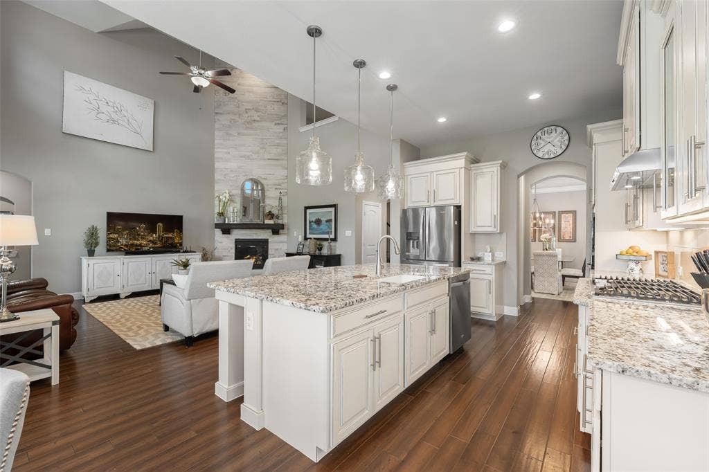 121 Lantana Lane, Wylie, TX 75098 Open concept kitchen and living area featuring a vaulted ceiling, wood-finish flooring, a stone-front fireplace, and an expansive kitchen island with a built-in sink