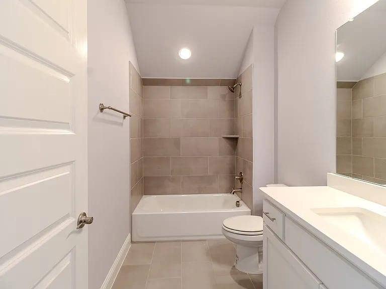 Bathroom featuring a white vanity with integrated sink, a rectangular mirror, a bathtub with tiled surround, and a built-in shower niche