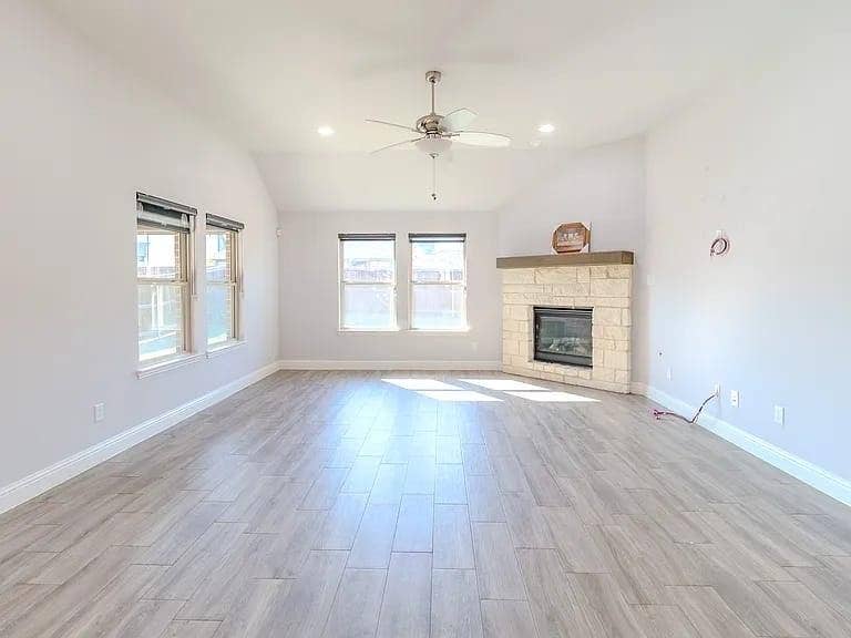 Vaulted ceiling with a ceiling fan, stone-clad fireplace with a wood mantle, recessed lighting, multiple windows, and tile flooring
