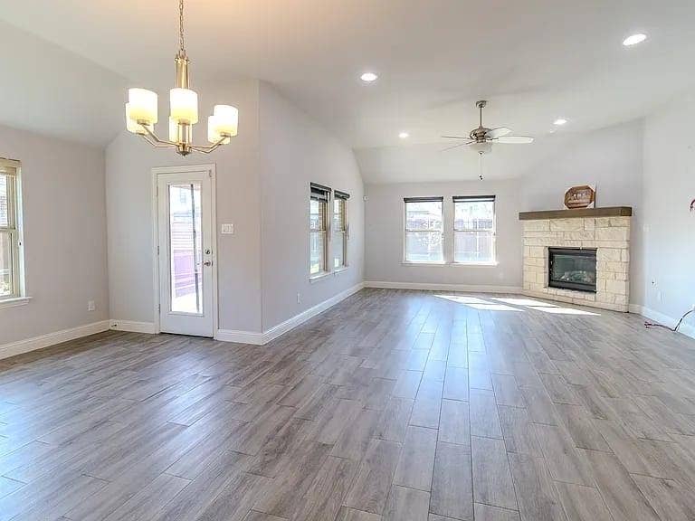 Spacious room featuring vaulted ceilings, recessed lighting, wood-finish flooring, a stone fireplace with a wood mantle, and multiple windows