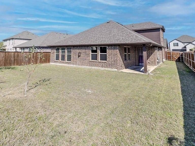 Brick exterior with multiple windows, covered patio, fenced perimeter, and a pitched shingle roof