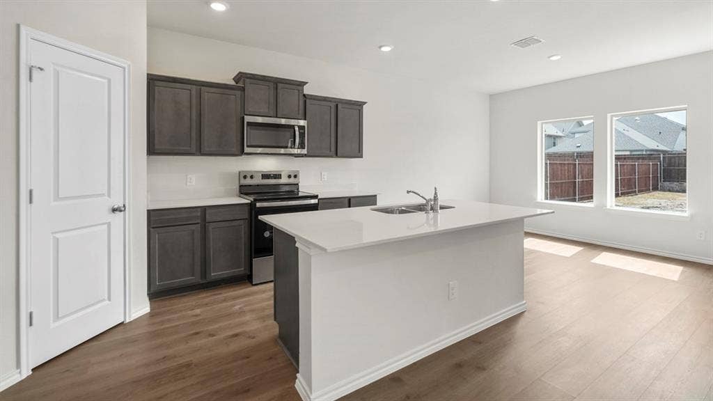 5610 Gannet Place, Crandall, TX 75114 Open-concept kitchen featuring dark wood cabinetry, stainless steel appliances, a white tile backsplash, and a central island with an undermount sink