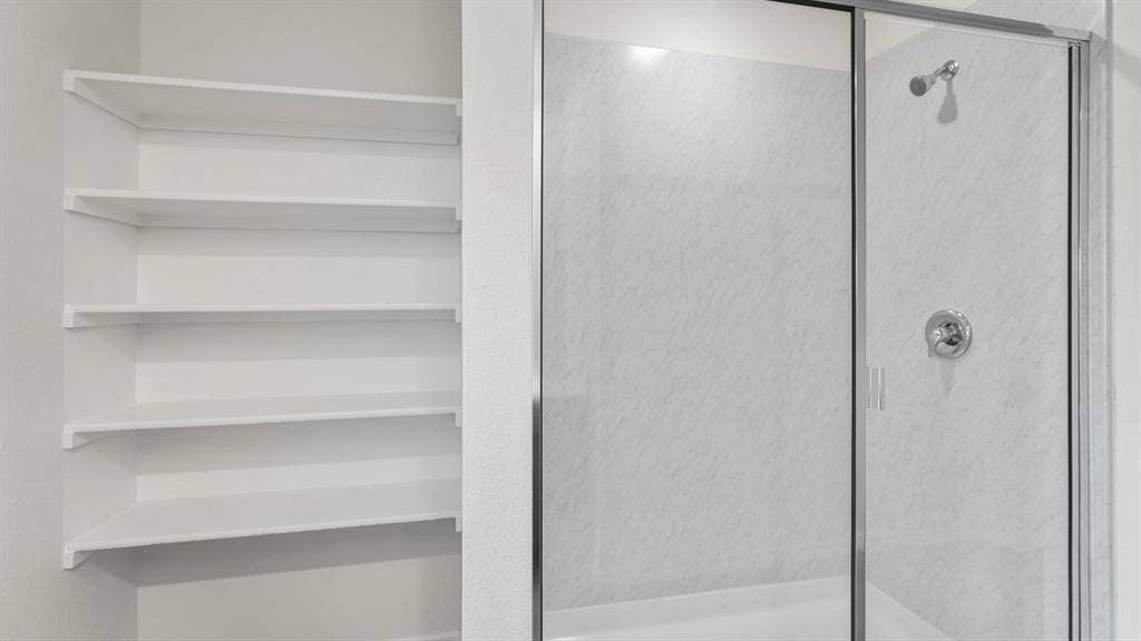 5610 Gannet Place, Crandall, TX 75114 Built-in shelving unit with multiple white shelves paired with a shower enclosure featuring a glass door, white surround, and chrome fixtures