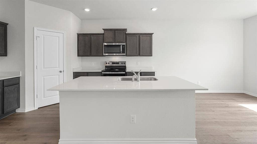 5610 Gannet Place, Crandall, TX 75114 Modern kitchen featuring a large island with an undermount sink, dark wood-finish cabinetry, stainless steel appliances, light countertops, and recessed lighting