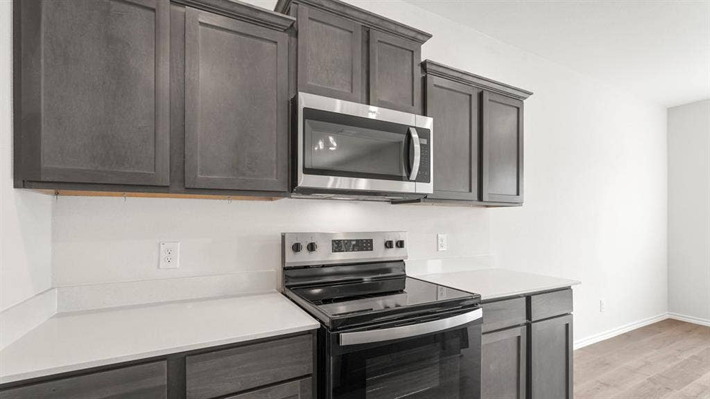 5610 Gannet Place, Crandall, TX 75114 Kitchen featuring dark wood-finish cabinetry, light countertops, white backsplash, stainless steel microwave, and electric range