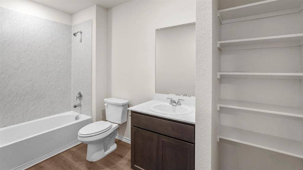 5610 Gannet Place, Crandall, TX 75114 Contemporary bathroom featuring a white tub with a textured surround, a dark wood-finish vanity with a white countertop and integrated sink, a wall-mounted mirror, and built-in shelving