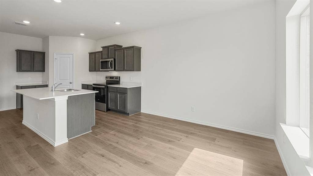 5610 Gannet Place, Crandall, TX 75114 Open-concept kitchen featuring dark gray cabinetry, white countertops, stainless steel appliances, a central island with an undermount sink, and wood-finish flooring