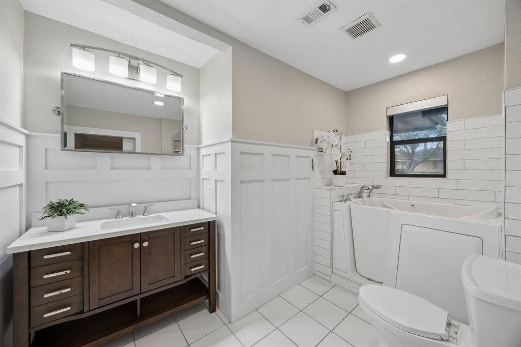 Guest bathroom with a spacious vanity, decorative wainscoting, subway tile and a walk-in soaking tub.