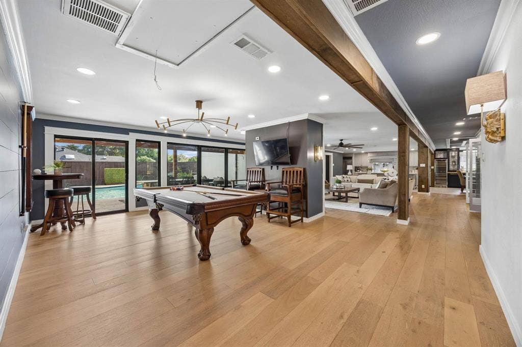 Spacious secondary living room currently used as a game room, featuring wood floors, modern lighting and a wall of windows overlooking the pool, with an open layout connecting to the main living areas.