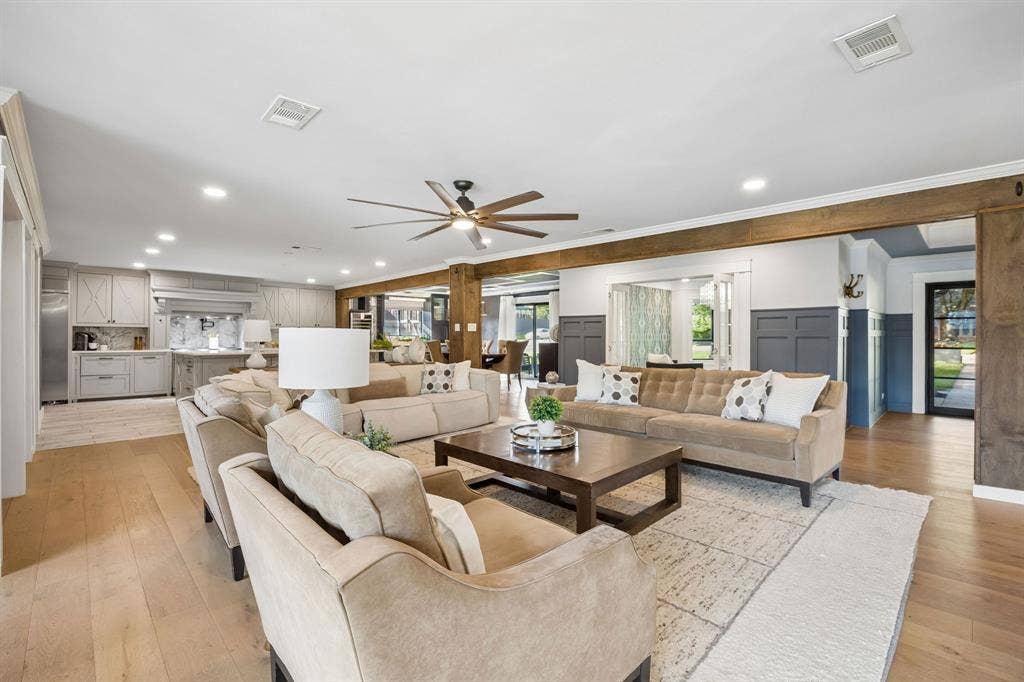 Spacious living room featuring wood floors, decorative wainscoting and exposed wood beams, with an open layout connecting to the kitchen, dining room and home office.
