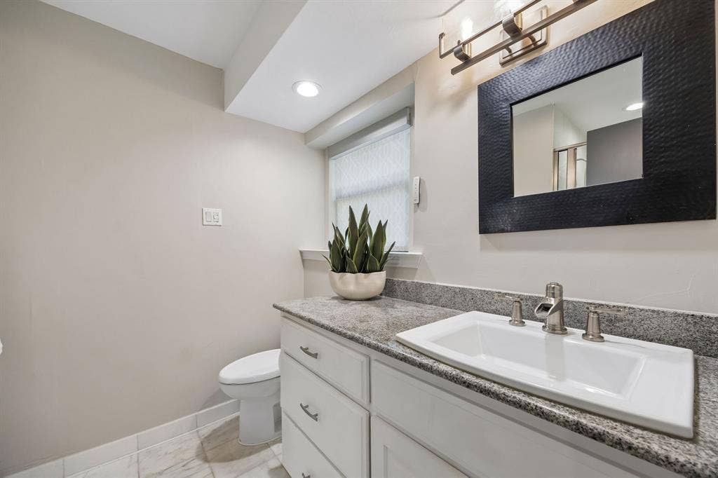 Secondary ensuite bathroom featuring a granite countertop, white cabinetry, decorative mirror, free standing shower and neutral finishes.