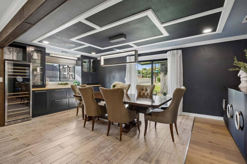Elegant dining room with a dramatic coffered ceiling, modern statement lighting, custom built-ins, wine refrigerator and abundant natural light.