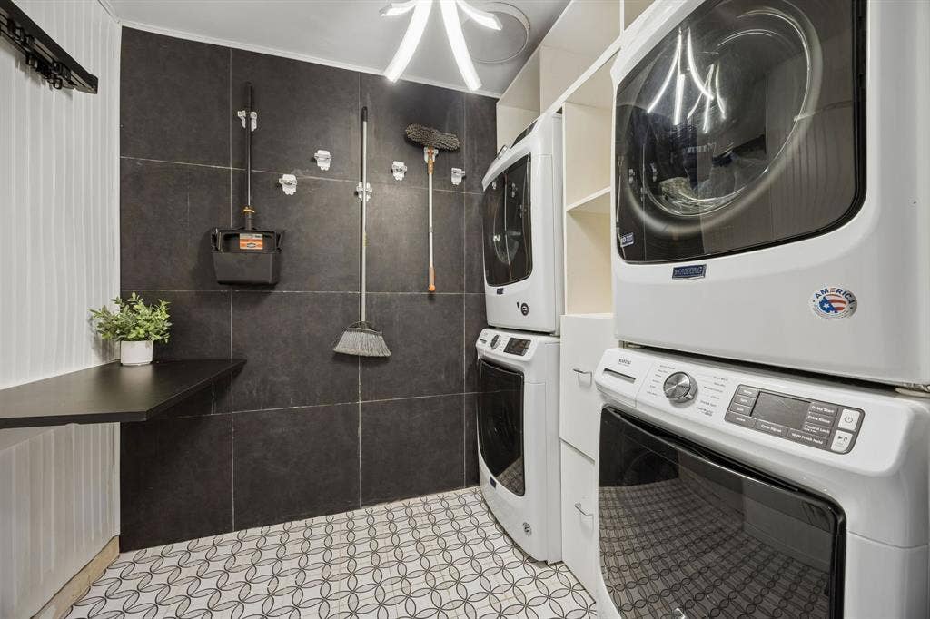 Well-appointed laundry room featuring two stacked washer and dryer sets, built-in storage, a folding counter and decorative tile flooring.