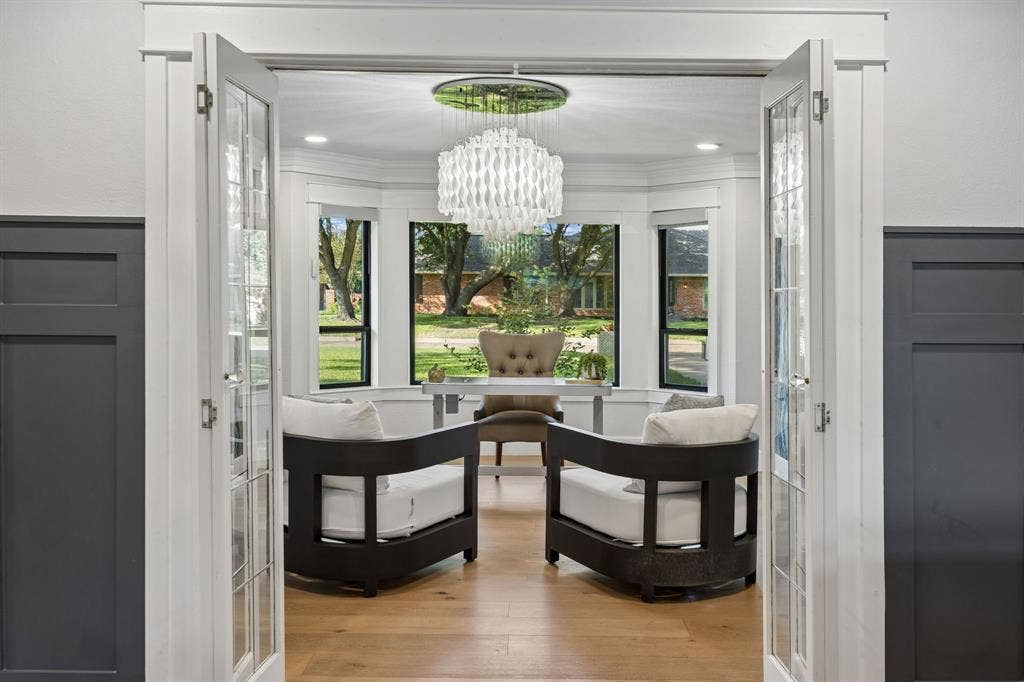 French doors open to the beautifully appointed home office, featuring a wall of windows, wood floors and a statement chandelier.